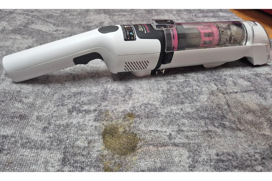 Der Shark Stainforce Akku-Fleckenreiniger liegt auf dem Teppich in Benutzung, man sieht das Handgerät.